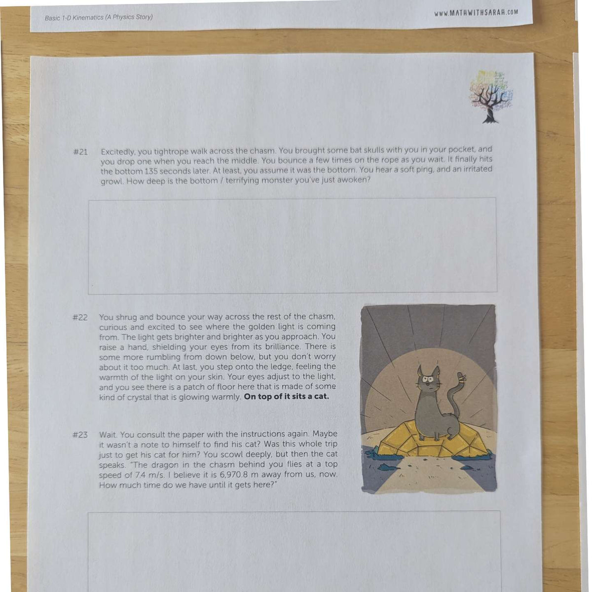 A printed worksheet page with three numbered physics questions, a small tree illustration, and a cartoon cat sitting in a basket, photographed on a wooden surface.