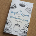 The book The Hopeful Queen of the Clockwork Court sitting on some fabric