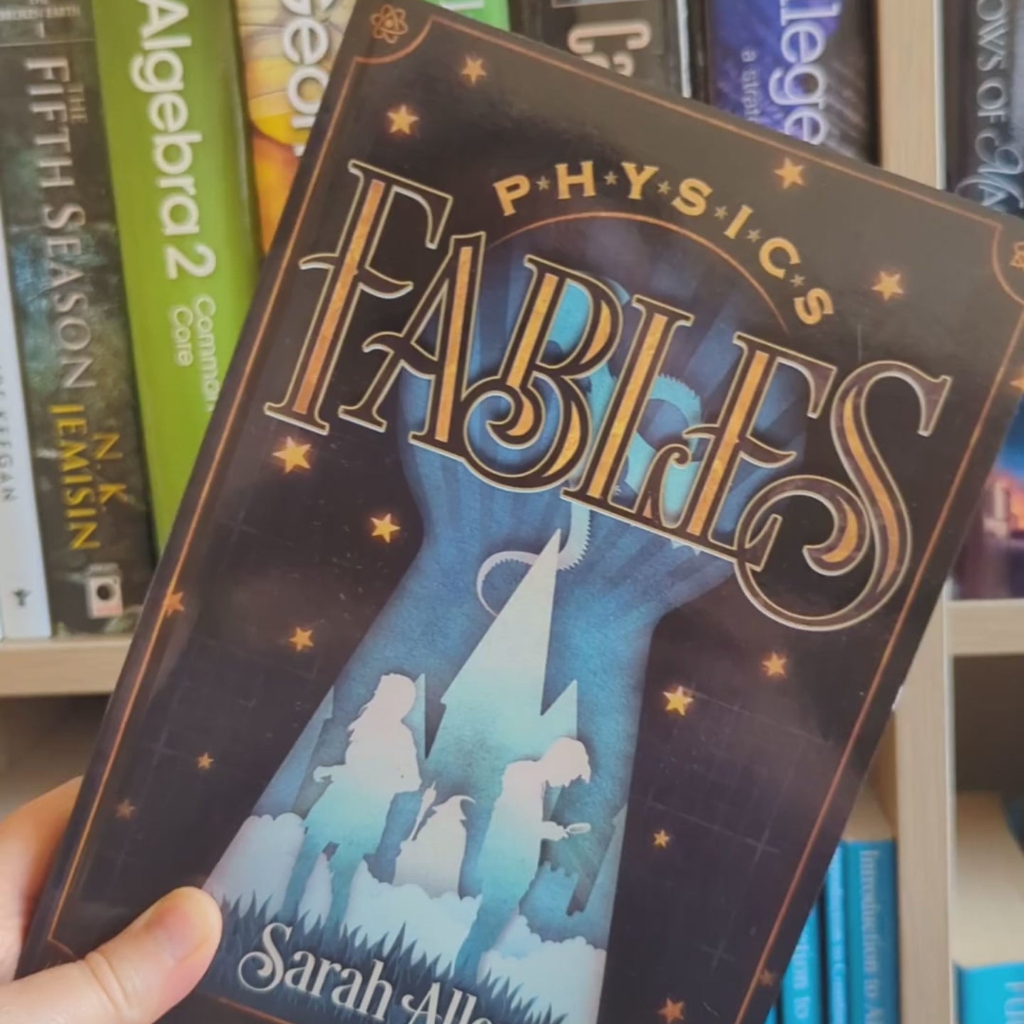 video showing physics fables rotating to show the spine about a third of an inch thick, in front of a shelf of math books
