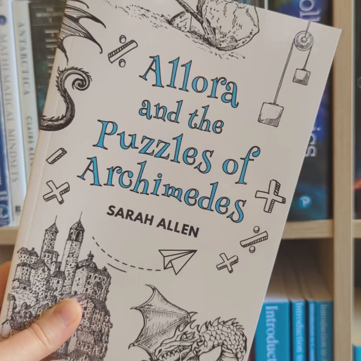 a video of the allora book rotating in front of a bookshelf. the spine is about half an inch thick