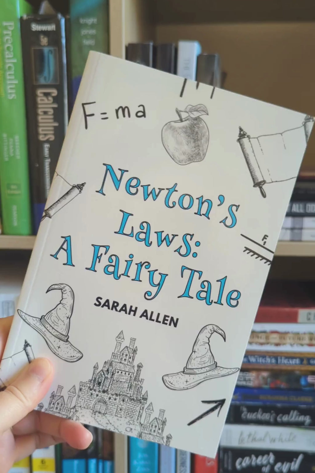a hand holding the newton's laws paperback in front of a bookshelf rotates it so you can see the spine is about a centimeter thick