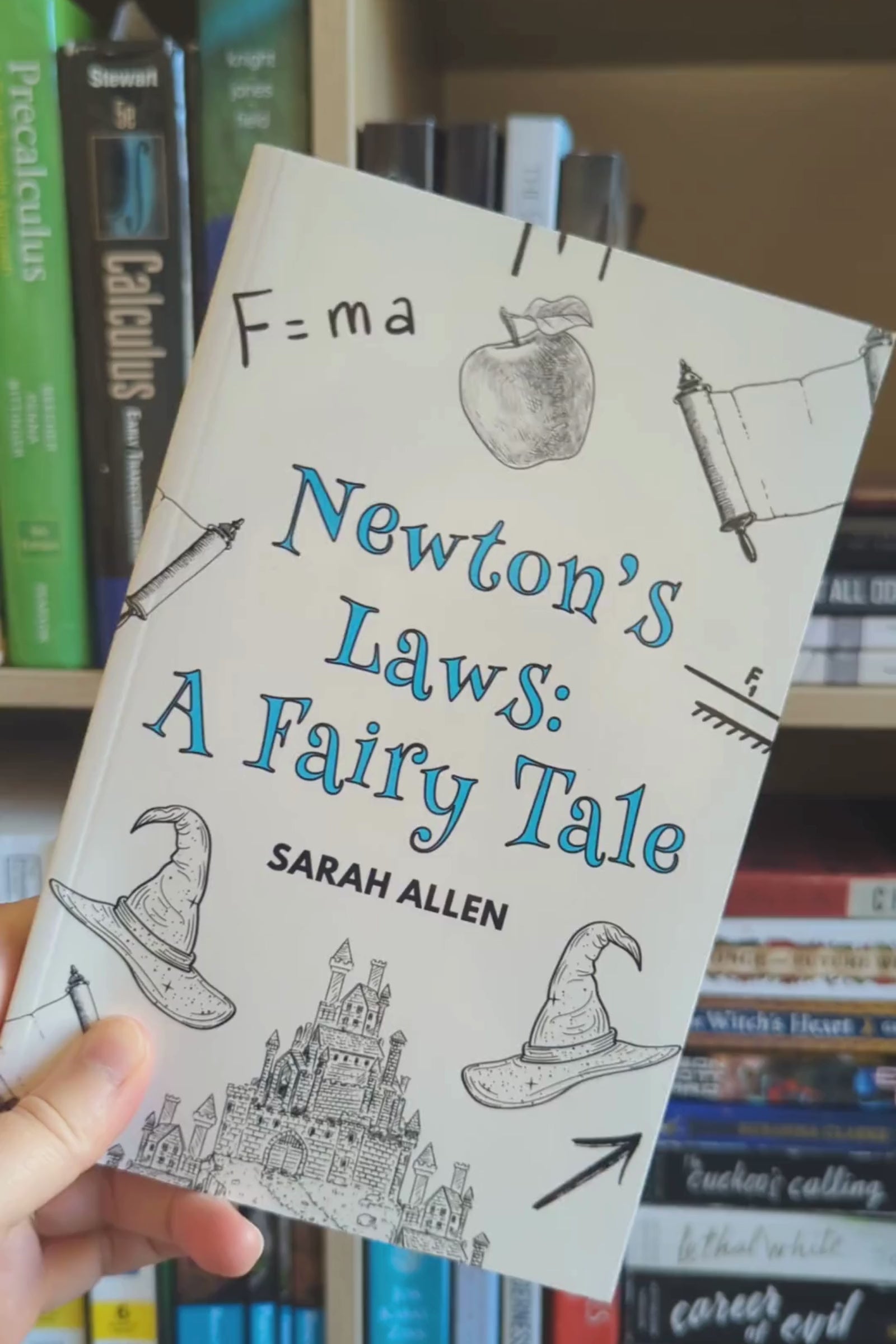 a hand holding the newton's laws paperback in front of a bookshelf rotates it so you can see the spine is about a centimeter thick